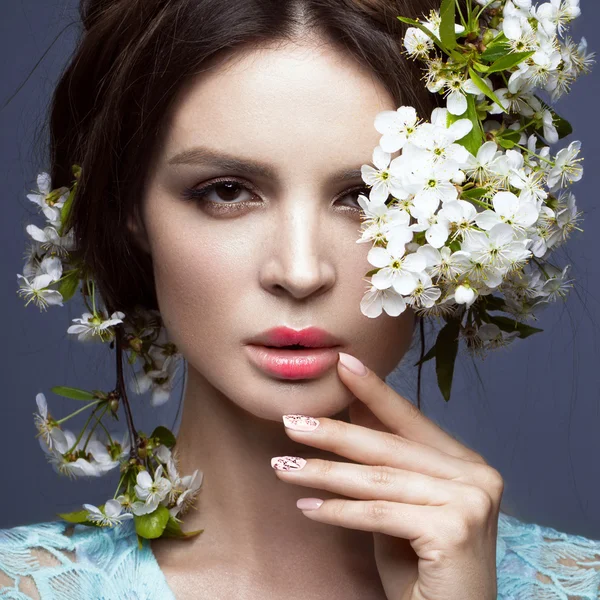 Vakker brunette jente i blå kjole med en forsiktig romantisk make-up, rosa lepper og blomster. Skjønnheten i ansiktet . – stockfoto