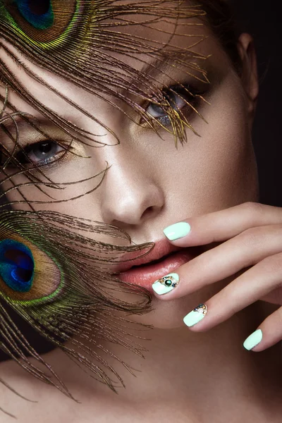 Menina bonita com maquiagem brilhante, design de manicure e pena de pavão em seu rosto. Unhas de arte . — Fotografia de Stock