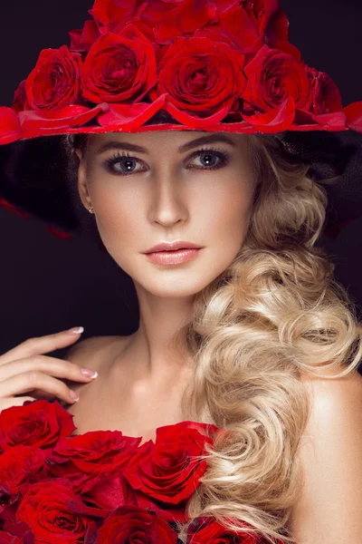 Schöne blonde Mädchen in Kleid und Hut mit Rosen, klassisches Make-up, Locken, rote Lippen. Schönheit Gesicht. — Stockfoto