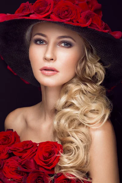 Mooi blond meisje in jurk en muts met klassieke make-up, krullen, rozen, rode lippen. Schoonheid gezicht. — Stockfoto