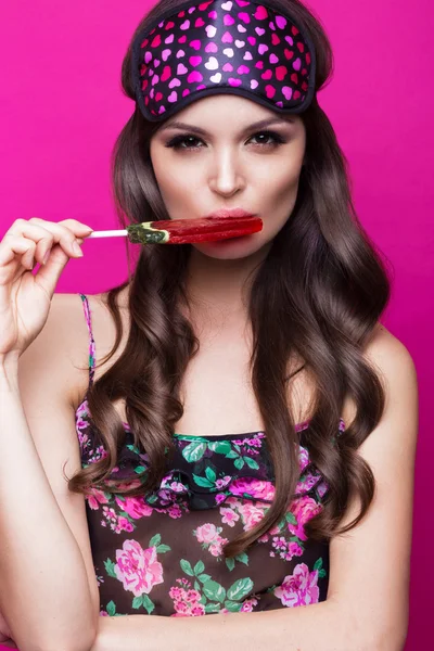 Забавная молодая женщина в маске и пижаме, сладости на розовом фоне. красота лица . — стоковое фото