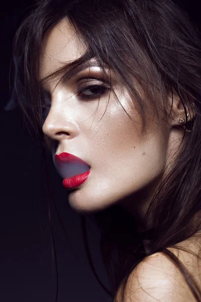 Mooie sexy brunette meisje met lichte make-up, rode lippen, rook uit de mond. schoonheid gezicht. — Stockfoto