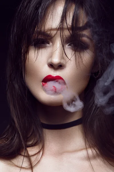 Krásná sexy tmavovláska s světlý make-up, červené rty, kouř z úst. krása obličej. — Stock fotografie