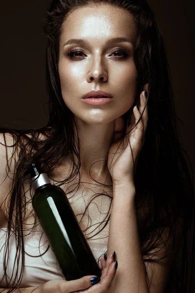 Menina bonita com uma maquilagem brilhante, cabelo molhado e pele, garrafa de produtos cosméticos nas mãos. Cara de beleza . — Fotografia de Stock