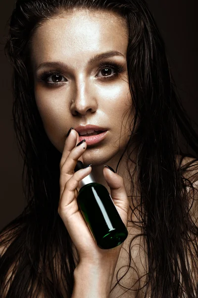 Schöne Mädchen mit einem hellen Make-up, nasse Haare und Haut, Flasche Kosmetikprodukte in den Händen. Schönheit Gesicht. — Stockfoto