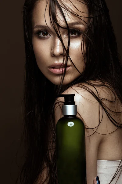 Piękna dziewczyna z jasny makijaż, wilgotne włosy i skórę, butelka produktów kosmetycznych w ręce. Piękna twarz. — Zdjęcie stockowe