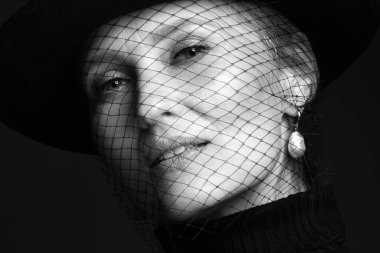 Yüzünde klasik makyaj ve peçe olan siyah gömlekli güzel yaşlı bir kadının portresi..