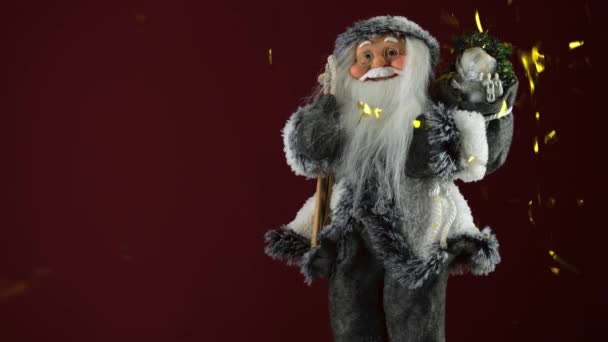 Brinquedo de Papai Noel em um fundo vermelho com lantejoulas de ouro voadoras. Feliz Natal e um feliz ano novo — Vídeo de Stock