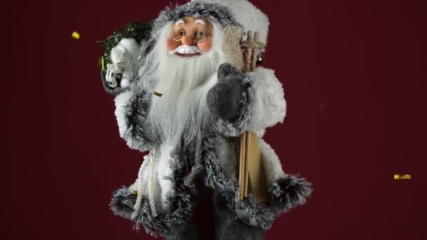 Santa Claus hračka na červeném pozadí s létající zlaté flitry. Veselé Vánoce a šťastný nový rok — Stock video