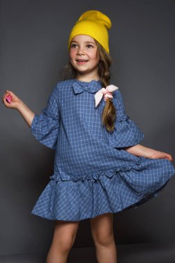 Küçük kız profesyonel olarak stüdyoda elbise ve sarı şapkayla poz veriyor. Model testleri