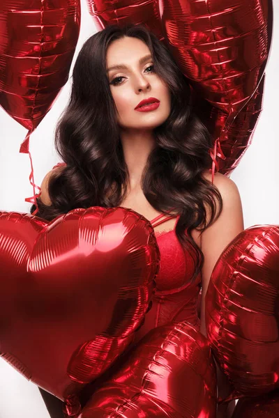 Сексуальная женщина в красном кружевном белье и воздушных шарах с сердечками позирует в студии на День Святого Валентина — стоковое фото