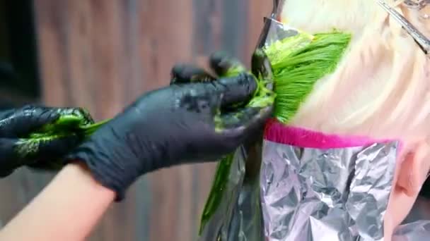 O cabeleireiro pinta o cabelo de uma mulher loira em diferentes cores brilhantes — Vídeo de Stock