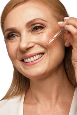 Portrait of a beautiful elderly woman in a white shirt with cosmetic face oil in her hands