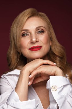 Beyaz gömlekli, güzel, yaşlı bir kadının portresi. Klasik makyaj ve sarı saçlı..