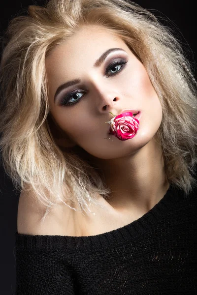Schöne blonde Mädchen mit dunklem Make-up mit einer Blume auf den Lippen. Schönheit Gesicht — Stockfoto