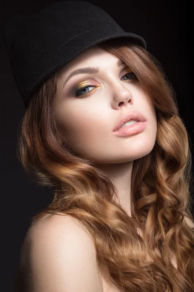 Vacker flicka med ljusa smink och lockar i en hatt. Skönhet ansikte. — Stockfoto