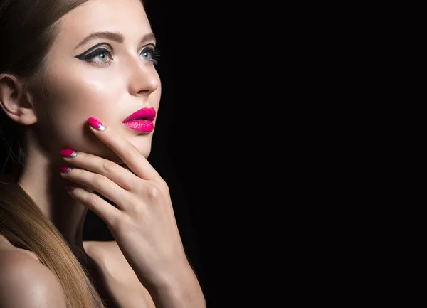 Beautiful girl with unusual black arrows on eyes and pink lips and nails. Beauty face. Picture taken in the studio on a black background. — Stock Photo, Image