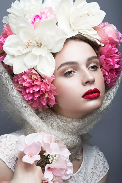 Menina bonita em um lenço de cabeça no estilo russo, com grandes flores na cabeça e lábios vermelhos. Cara de beleza . — Fotografia de Stock
