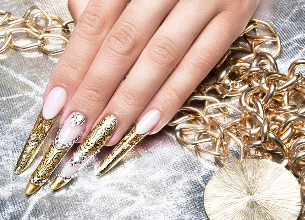 Beautiful long nails in a gold design with rhinestones. Nail art.