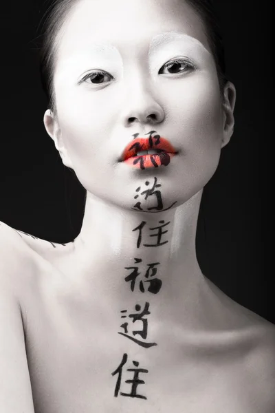 Vacker asiatisk tjej med vit hud, röda läppar och hieroglyferna på hennes ansikte. Konst skönhet bild. — Stockfoto