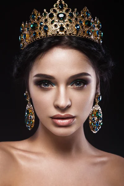 Bella ragazza bruna con una corona d'oro, orecchini e trucco serale professionale. Bellezza viso . — Foto Stock