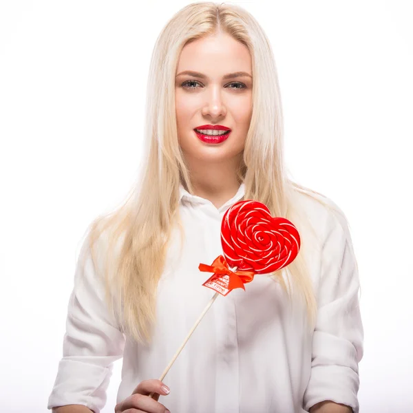 Retrato de hermosa mujer rubia con maquillaje brillante y corazón de caramelo rojo en la mano. día de San Valentín —  Fotos de Stock