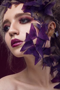 Creative fashionable image, girl with a bright make-up and purple plant on her face.