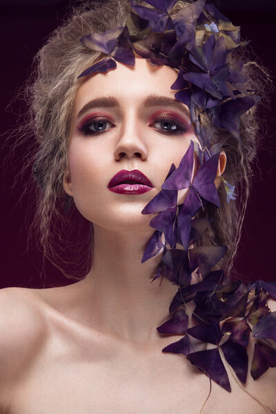 Creative fashionable image, girl with a bright make-up and purple plant on her face.