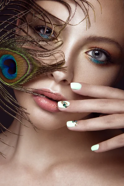 明るい化粧品で美しい少女は、彼女の顔にマニキュア デザインと孔雀の羽。爪のアート. — ストック写真