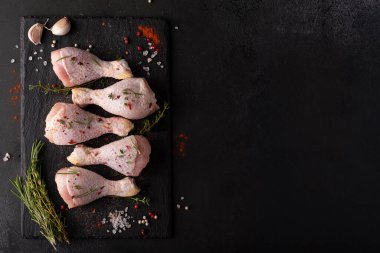 raw chicken drumsticks with spices and herbs on black board, top view