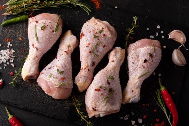 raw chicken drumsticks with spices and herbs on black board, top view