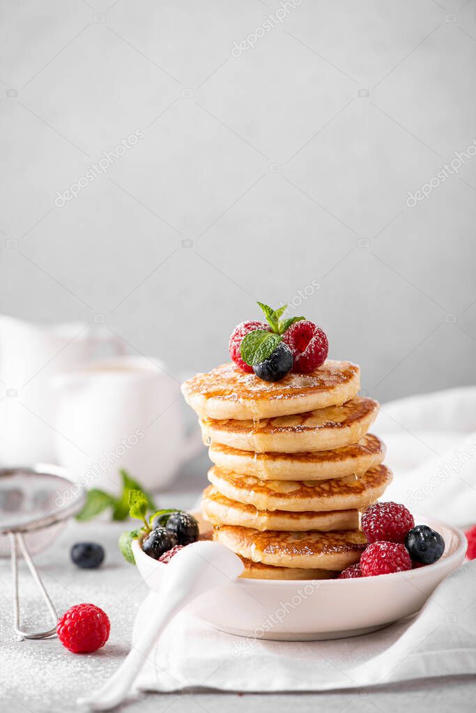 homemade pancakes with fresh berries and honey on a white plate, close-up