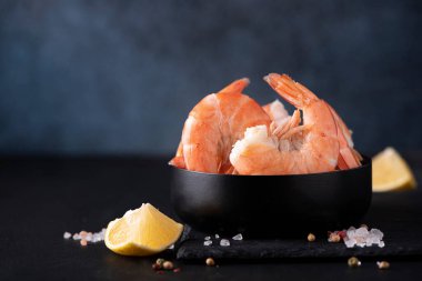 Siyah bir kasede limonlu kabuklu haşlanmış karides, yakın plan.