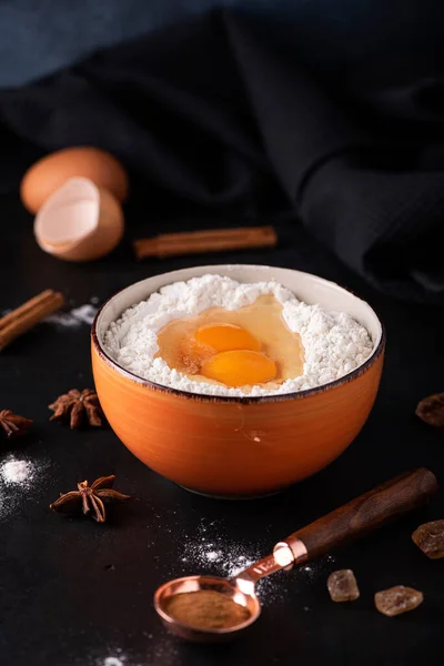 ingredients for the pie - flour, eggs, sugar, cinnamon in an orange bowl on a dark background