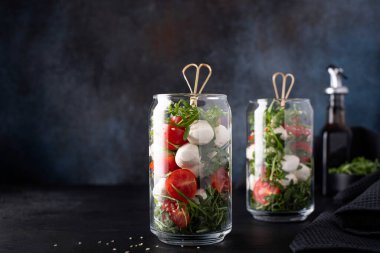 Çeri domatesli mozzarella ve koyu arkaplanda cam bir kavanozda roka.