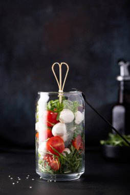Çeri domatesli mozzarella ve koyu arkaplanda cam bir kavanozda roka.