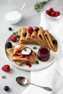 Gri tabakta taze böğürtlenli ve reçelli ince tatlı krepler, yakın plan.