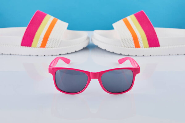 Summer travel concept. Flip flops or slippers and sunglasses on a pastel background. Beach accessories.