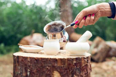 Sıcak bir şeyler içelim. Doğada baharatlı kahve pişirme süreci. Arka plan - kamp ve orman.