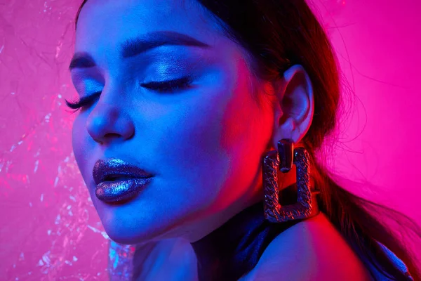 Stüdyodaki neon ışıklarda metalik gümüş dudaklı ve arka planda şeffaf film olan bir kadın. Sanat tasarımı.