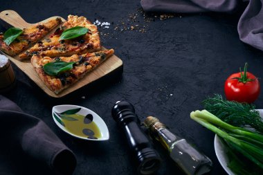 İtalyan pizzası ve pizza pişirme malzemeleri arka planda. Domates, zeytin yağı, otlar ve baharatlar..