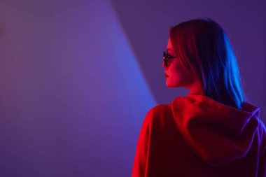 Moda mankeni kapüşonlu ve gözlüklü bir genç bayan stüdyo arka planında güneş gözlüğü takıyor. Kapat..