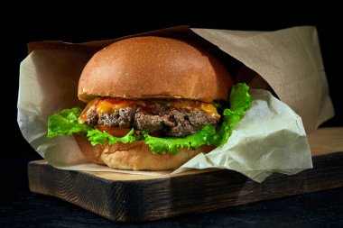 Tahta tahtada kahverengi eko kağıt paketli hamburgerler ve karanlık bir arka plan..