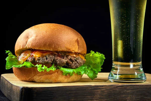Fast food and Cold light beer. Burger placed on a wooden board on bar counter with copy space.