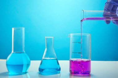 Mavi arka planda renk sıvısı olan farklı bir laboratuvar bardağı. Laboratuvar kimyasal araştırmaları için renkli sıvılarla test tüpleri..