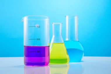 Mavi arka planda renk sıvısı olan farklı bir laboratuvar bardağı. Laboratuvar kimyasal araştırmaları için renkli sıvılarla test tüpleri..