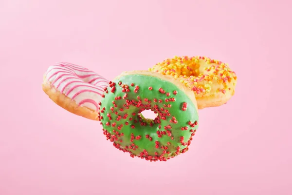 Mix of Different doughnuts with sprinkles on pink pastel background. Sweet donut falling or flying in motion. Close up.