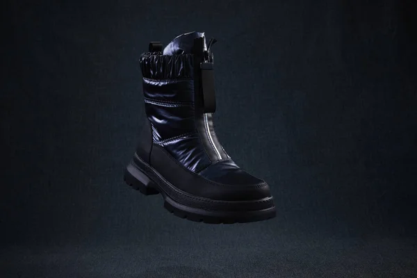 Fashion black unbranded boot flying on dark background. Black winter walking shoes levitate in air. Modern female shoes for off-road walking.