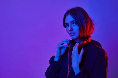 Moda hippisi kadın şık gözlükler takıyor ve kulaklık takıyor. Stüdyoda neon renkli arka planda müzik dinliyor..