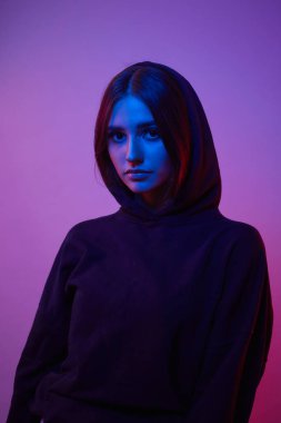 Moda neon ışıklarıyla bir stüdyoda poz veren kız. Renkli ışık efektleri olan kapüşonlu kadın..